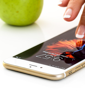 A hand touching a smartphone with an apple in the background