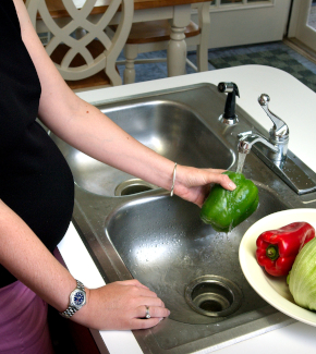 A pregnant woman washes vegetables before cooking.