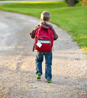 A child with a schoolbag on, walking down a driveway