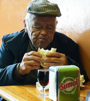 An elderly man eating a sandwich in a bar