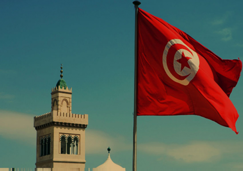 bandera de Túnez en primer plano y minarete de una mezquita en el segundo