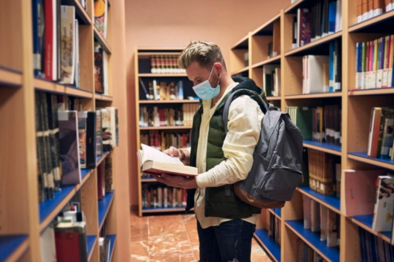 Estudiante consulta un libro en una biblioteca universitaria
